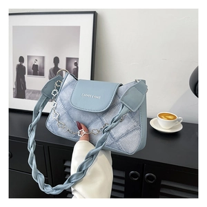 Detail of light blue denim underarm bag featuring twisted strap and floral metal chain