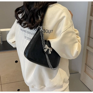 Rear view of a black leather underarm bag with silver bow and chain detail on a model