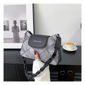 Detail of grey denim shoulder bag featuring a black leather flap and floral chain strap