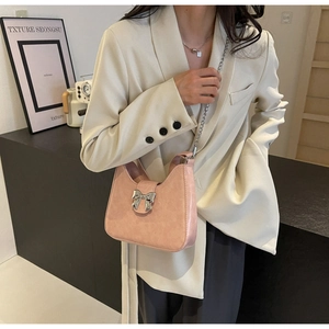 Pink shoulder bag with silver bow buckle and chain strap shown on model's shoulder