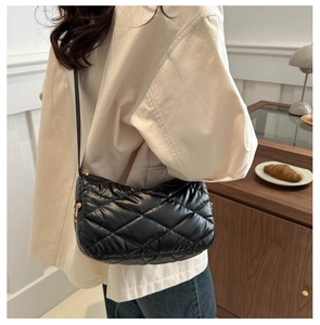 Détail d'un sac bouffant noir matelassé avec fermeture éclair dorée porté en bandoulière