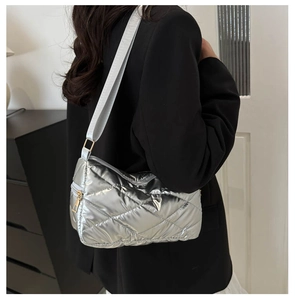 Détail du sac bandoulière argenté matelassé avec large sangle sur un blazer noir