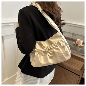 Detail view of champagne satin shoulder bag with pleated handle and decorative bow knot