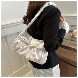 Detail view of a white pleated satin shoulder bag with bow drawstring on a model
