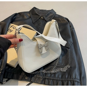 Detail of white leather shoulder bag featuring a silver metal bow and detachable chain