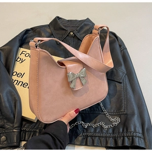Detail of pink crescent bag with silver metallic bow and chain strap on leather jacket