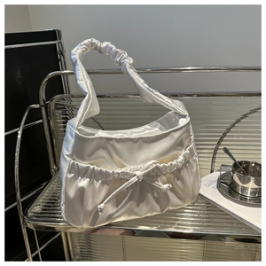 Detail of white satin pleated underarm bag with drawstring bow on a metal display stand
