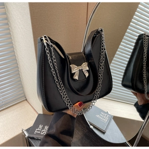 Detail of a chic black baguette bag with silver bow ornament and metallic chain strap