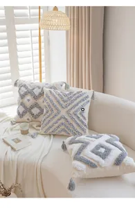 Detail of Nordic cream tufted pillows with geometric grey patterns and soft fringe tassels