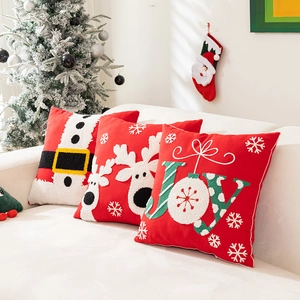 Tres cojines navideños con Papá Noel, reno y letras JOY bordadas sobre sofá blanco
