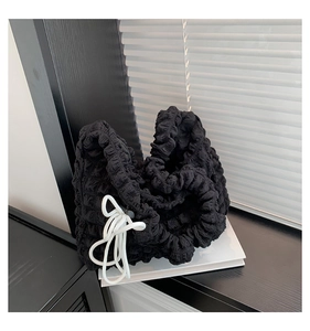 Detail of black cloud bag featuring pleated texture and white decorative drawstrings