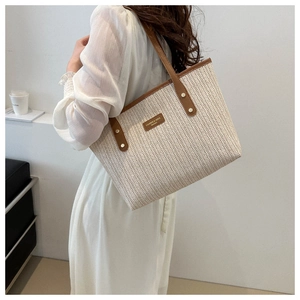 Detail of woven straw tote bag with brown leather handles and brand nameplate on model