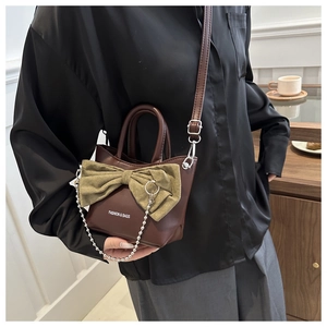 Detail of a brown leather handbag with a large green bow and silver bead chain strap