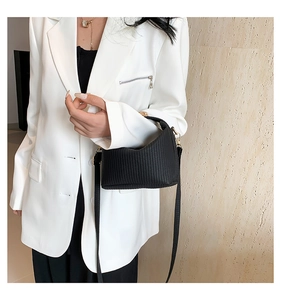 Détail du mini sac plissé noir avec boucles dorées porté sur un blazer blanc