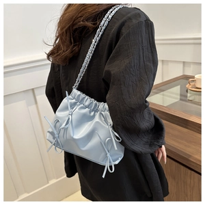 Détail du sac seau bleu clair à chaîne avec nœuds décoratifs sur une tenue noire