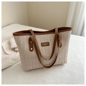 Close-up of woven straw tote with brown leather handles and brand name nameplate detail
