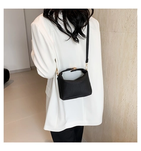 Sac à main plissé noir chic avec fermoir doré sur un costume blanc pour un look minimaliste