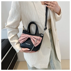Detail of a chic black handbag with a large pink bow and metal chain on a model