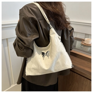 Detail of white pleated shoulder bag with metallic butterfly buckle and chain strap on model
