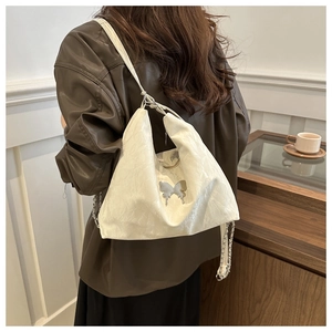 Detail of white tote bag with silver bow ornament and chain strap on shoulder
