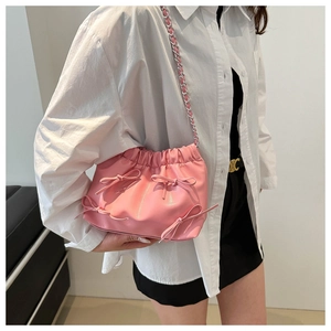Sac seau rose plissé avec nœuds et bandoulière chaîne argentée porté par un mannequin