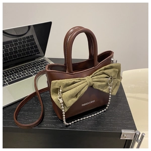 Close-up of brown PU leather handbag featuring a large green bow and silver chain detail
