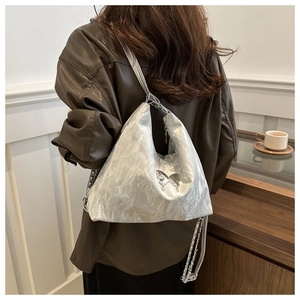 Close-up of metallic silver pleated tote bag featuring a metal butterfly and chain strap