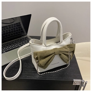 Detail of white handbag with large green fabric bow and silver metal chain accessory