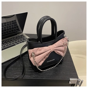 Detail of black shoulder bag featuring a large pink bow, silver bead chain and logo print