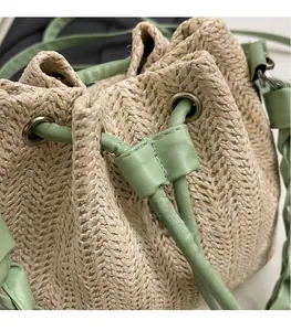 Close-up of woven straw bucket bag featuring beige texture and green leather drawstring detail