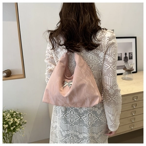 Detail of pink pleated shoulder bag with silver butterfly accent on model with white dress