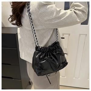 Détail du sac seau noir plissé avec nœuds décoratifs et bandoulière en chaîne mode