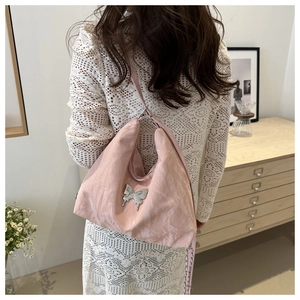 Detail of pink shoulder bag with silver butterfly emblem and pleated fabric texture