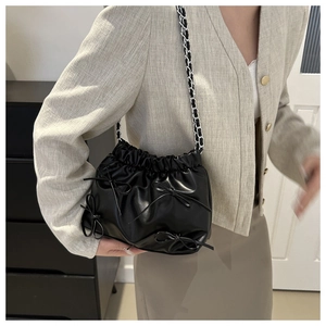 Détail d'un sac seau noir plissé avec des nœuds et une bandoulière en chaîne argentée