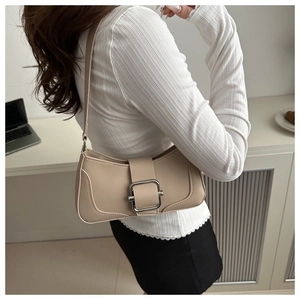 Close-up of beige underarm bag with silver buckle worn on shoulder in office setting