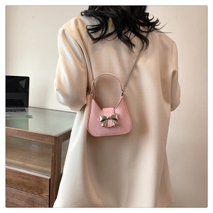 Détail du mini sac rose avec nœud argenté porté en bandoulière sur une veste beige