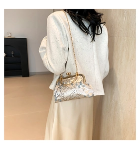 Detail of vintage frame bag with blue floral embroidery and gold chain on white jacket