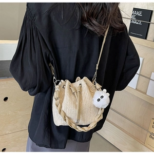 Detail of beige woven bucket bag with leather handle, crossbody strap and white pompom charm