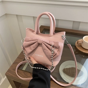 Pink shoulder bag with large bow and silver bead chain on a minimalist wooden table
