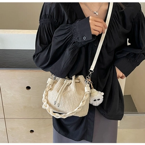 Detail of woven straw bucket bag texture with plush charm and wide shoulder strap