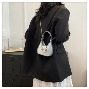 Gros plan d'un mini sac argenté avec boucle en nœud métallique et bandoulière chaîne