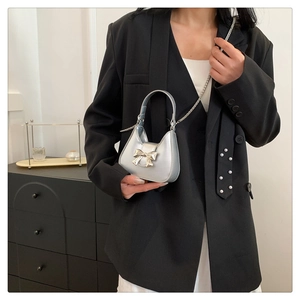 Mini sac argenté avec nœud et chaîne en métal porté par un mannequin en costume noir