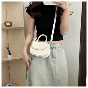 Close-up of minimalist white saddle bag with curved flap and adjustable crossbody strap