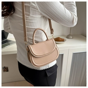 Close-up of minimalist apricot saddle bag with adjustable strap and gold metal hardware