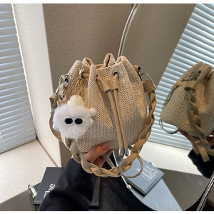 Detail of woven bucket bag with drawstring closure and cute plush doll pendant