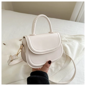Close-up of minimalist cream white PU leather saddle bag with gold metal hardware detailing