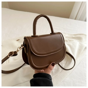 Detail of a brown faux leather saddle bag featuring a round handle and crossbody strap