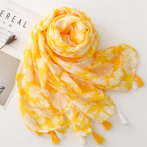 Detail of yellow cotton scarf with white daisy floral print and fringe tassels on white desk