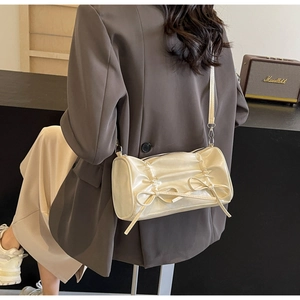 Detail of cream pleated cylindrical bag with ribbon accents and metallic shoulder hooks