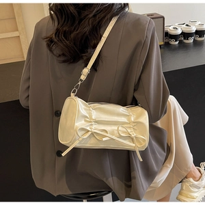 Detail of cream white pleated cylinder bag with decorative bows and adjustable strap